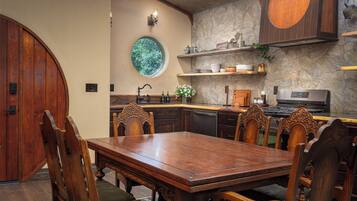 Zona pranzo con tavolo e sedie in legno, parete in pietra e finestra circolare.
