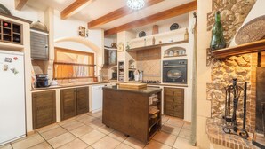 Una cocina con isla central, armarios de madera, horno empotrado y pared de piedra.