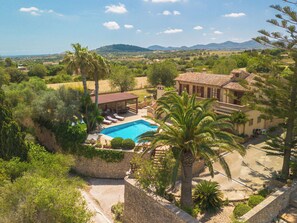 Eine Villa mit Swimmingpool, umgeben von üppiger Vegetation und Blick auf ferne Hügel.