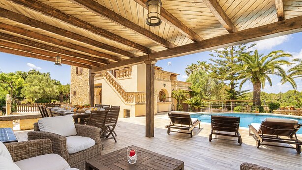 Un patio exterior con mobiliario de mimbre, una piscina y un edificio de piedra al fondo.