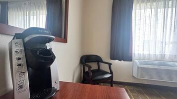 A hotel room with a coffee maker, a chair, and an air conditioning unit.