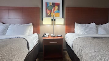 A hotel room with two beds, a nightstand with a lamp, a phone, and a framed artwork on the wall.