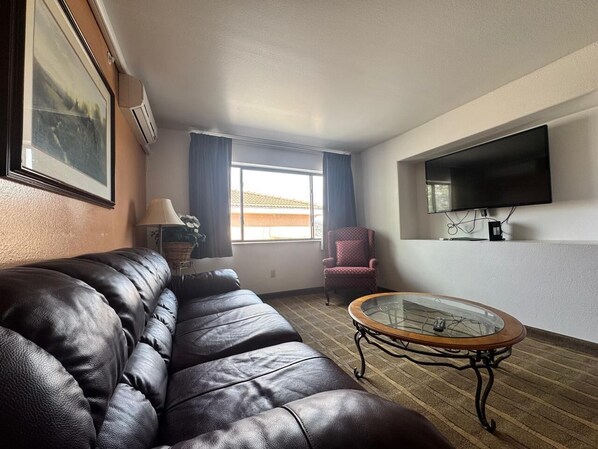 A living room with a leather sofa, a glass coffee table, a chair, a TV, and a window with curtains.