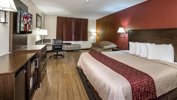 Ein Hotelzimmer mit Bett, Schreibtisch, Stuhl, Fernseher und einer roten Akzentwand.