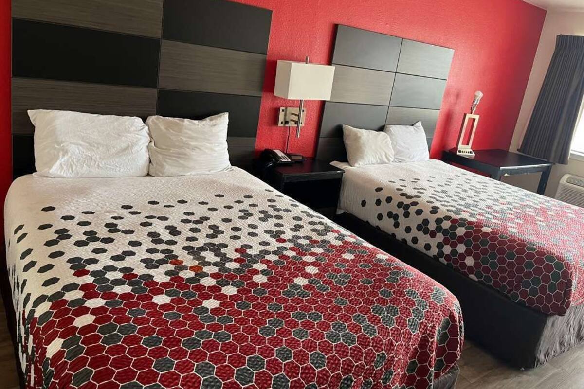Habitación de hotel con dos camas, cada una con una colcha estampada, cabeceros, mesitas de noche, lámparas y mesitas auxiliares.