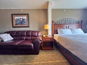 A hotel room with a leather sofa, a bedside table with a lamp, and a bed with white bedding. - FairBridge Inn & Suites Thermopolis (Thermopolis)