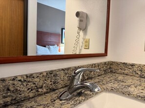 A bathroom with a granite countertop, a chrome faucet, and a hair dryer mounted on the wall.