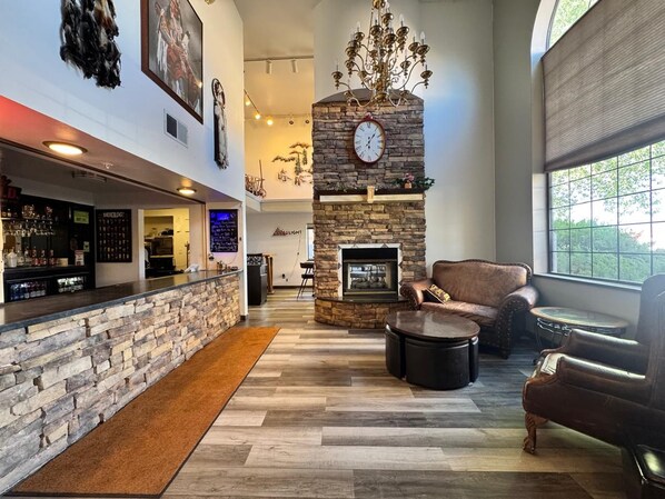 A bar area with a stone wall, a fireplace, leather seating, and a large window.