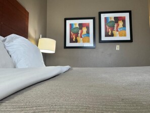 A hotel room with a bed, a nightstand with a lamp, and two framed artworks on the wall.