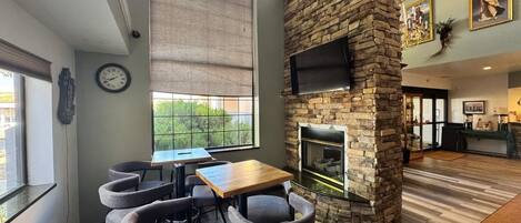 Un comedor con chimenea de piedra, un ventanal grande y un reloj en la pared.