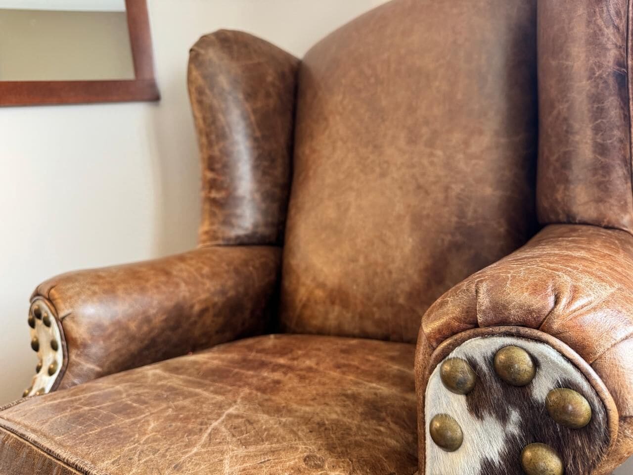 A brown leather armchair with a high backrest and armrests, featuring decorative metal studs.
