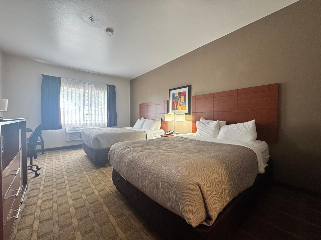 A hotel room with two beds, a desk, and a chair.
