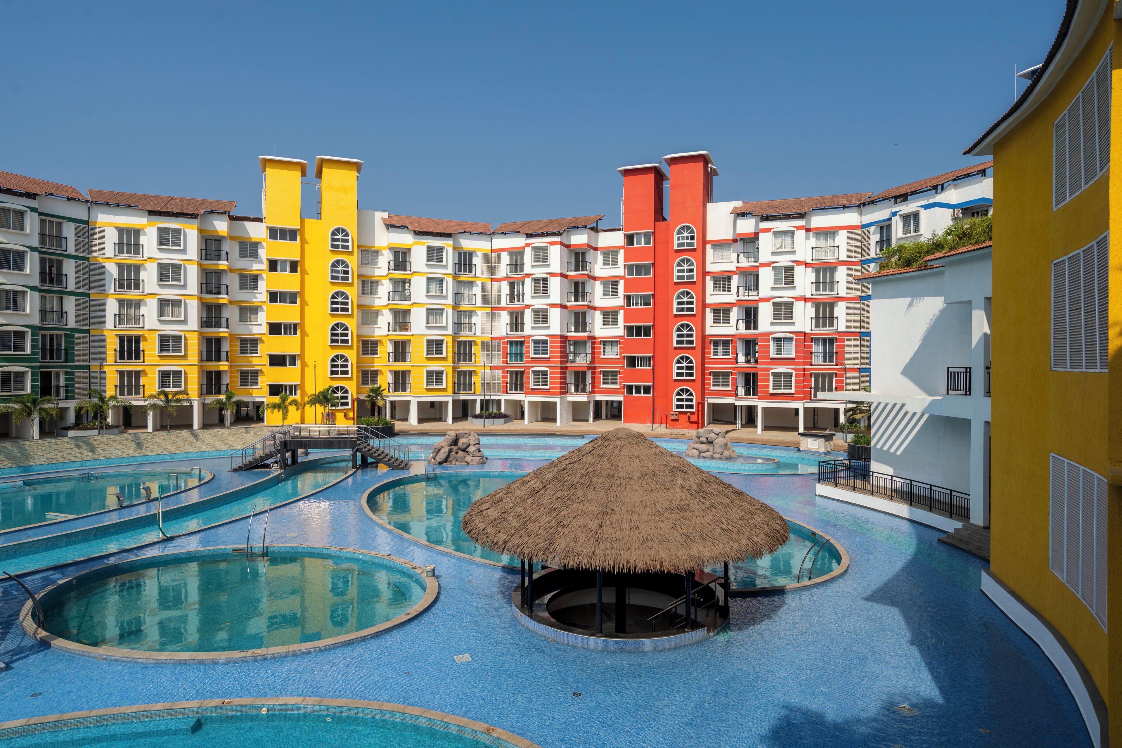 Un hôtel doté de plusieurs piscines, d’une piscine centrale de forme circulaire et d’une structure surmontée d’un toit de chaume.