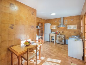 A compact kitchen with a wooden table, chairs, a refrigerator, an oven, and a microwave. - Dofins Bahia Azul by Interhome (Llucmajor)