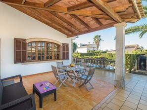 A covered patio with a wooden ceiling, a table with chairs, a small table with a purple tablecloth, and a window with shutters. - Dofins Bahia Azul by Interhome (Llucmajor)