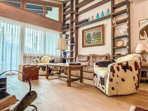 Ein gemütliches Wohnzimmer mit Holzboden, einer Couch, einem Couchtisch und einem Bücherregal.