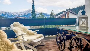Eine Holzdielen-Terrasse mit Tisch, Stühlen, einer Laterne und Blick auf schneebedeckte Berge.