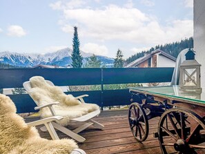 Eine Holzdielen-Terrasse mit Tisch, Stühlen, einer Laterne und Blick auf schneebedeckte Berge.