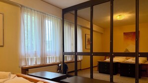 Ein Hotelzimmer mit Bett, Schreibtisch, Stuhl, Spiegel und einem Fenster mit Vorhängen.