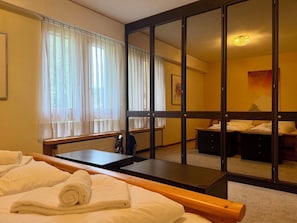 Ein Hotelzimmer mit Bett, Schreibtisch, Stuhl, Spiegel und einem Fenster mit Vorhängen.