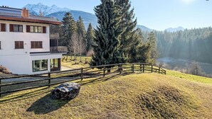 Een modern huis met balkon, houten omheining en uitzicht op besneeuwde bergen.