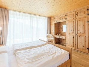 A bedroom with two beds, wooden cabinets, a chair, and a mirror. - Panorama Salums by Interhome (Laax)