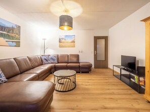 Uma sala de estar moderna com um sofá modular, uma mesa de centro redonda, uma televisão e uma estante.