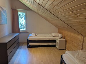 A bedroom with a sloped ceiling, a bed, a bedside table, a dresser, and a window with curtains. - Val Signina 3-28 by Interhome (Laax)