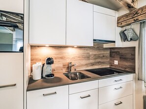 Eine moderne Küche mit weißen Schränken, einer Holzrückwand, einer Edelstahlspüle und einer Kaffeemaschine.