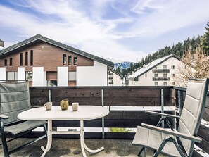 Ein Sitzbereich im Freien mit Tisch und Stühlen, einem Holzzaun und modernen Gebäuden im Hintergrund.