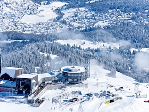 Ein Skigebiet mit einem kreisförmigen Gebäude, einer Seilbahn und verschneiter Landschaft.