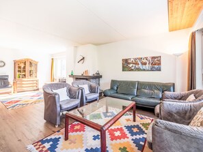 Ein Wohnzimmer mit einer Couch, Sesseln, einem Couchtisch, einem Schrank und einem Bild an der Wand.