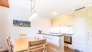 A modern kitchen with wooden cabinets, a central island, and a dining area with a wooden table and chairs. - Val Signina 4-8 by Interhome (Laax)