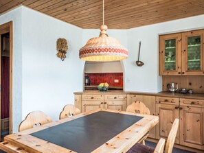 A wooden dining table with chairs, a hanging light fixture, and wooden cabinets. - Val Signina 8-18 by Interhome (Laax)