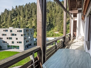A balcony with a view of a modern building and a forested area. - Val Signina 8-18 by Interhome (Laax)