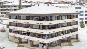 A multi-story building with balconies, a covered outdoor area, and a snowy landscape. - Quadra B223 by Interhome (Flims)