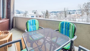 A balcony with two chairs and a table, overlooking a snowy landscape with buildings. - Quadra B223 by Interhome (Flims)