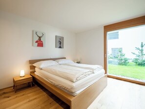 A bedroom with a wooden bed, a nightstand with a lamp, and two wall-mounted pictures. - Casa Miraselva by Interhome (Flims)