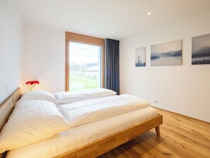 Una camera da letto moderna con un letto grande, una finestra vista su un paesaggio verde e due dipinti con paesaggi alle pareti.