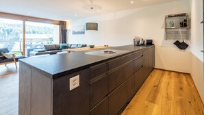 Cozinha moderna com ilha central, soalho de madeira e vista para varanda com mobiliário de exterior.