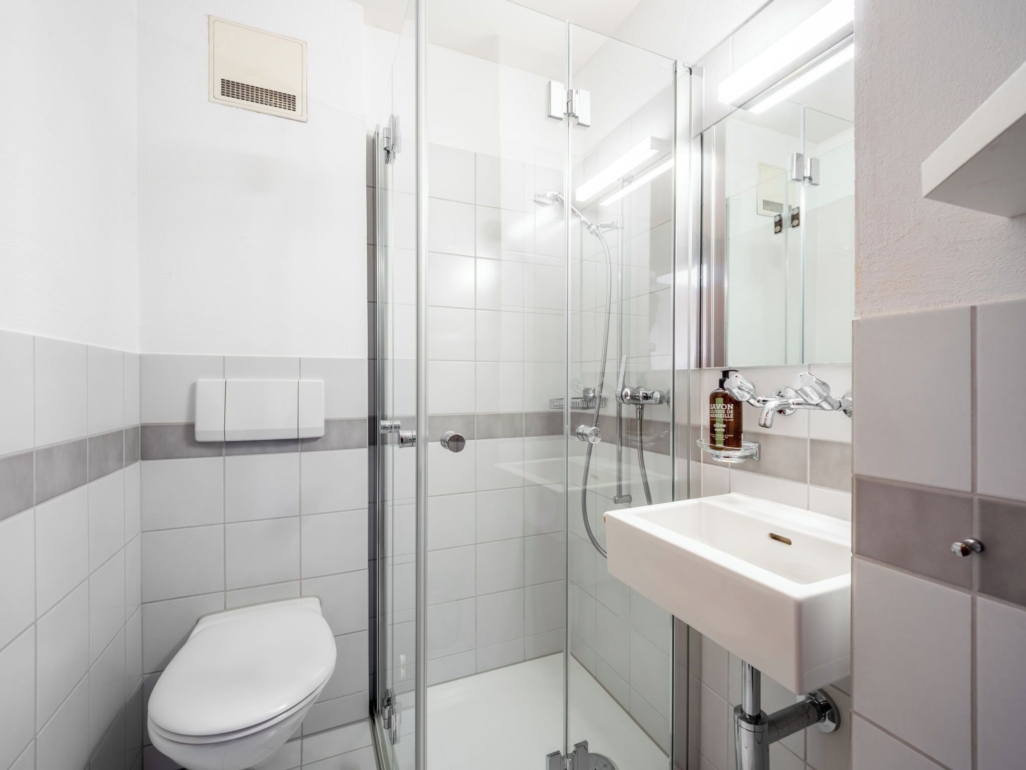 A modern bathroom with a glass-enclosed shower, a white toilet, and a sink with a mirror above it.