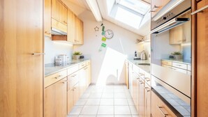 Een smalle keuken met houten kastjes, een roestvrijstalen oven en een dakraam.