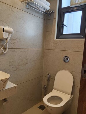 A small bathroom with a toilet, a towel rack, and a shower. - emersion residency (PUNE)