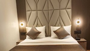 Uma cama grande com cabeceira geométrica, duas luminárias de mesa e um telefone no criado-mudo.
