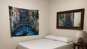 Una camera da letto con un letto, una ventola a soffitto, un comodino con una lampada e due opere d'arte alle pareti.