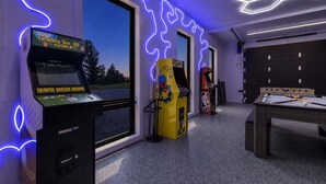 Quarto com jogos de fliperama, mesa de bilhar e janela com vista para árvores.