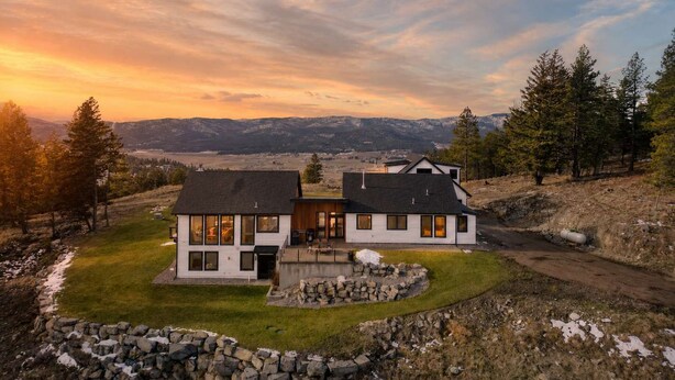 Uma casa de dois andares com alicerce de pedra, um muro de suporte de pedra e vista para a paisagem ao redor.
