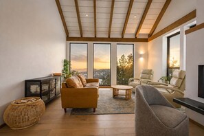 A spacious living room with a high ceiling, large windows offering a view of the outdoors, and a cozy seating area with a sofa and chairs.