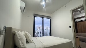A bedroom with a bed, a window with a city view, an air conditioning unit, and a door leading to another room. - Modern Apartments at the Hub City views (Panamá)