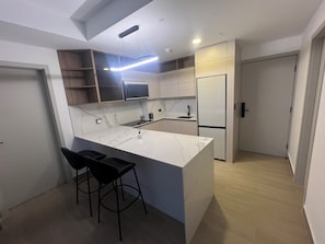 A modern kitchen with a marble countertop, black bar stools, a built-in microwave, and a refrigerator. - Modern Apartments at the Hub City views (Panamá)